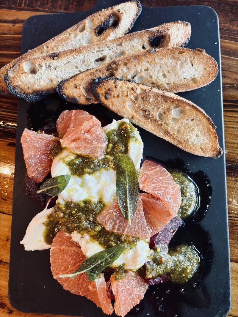 Fresh burrata with pesto, citrus, and toasted bread on a slate plate