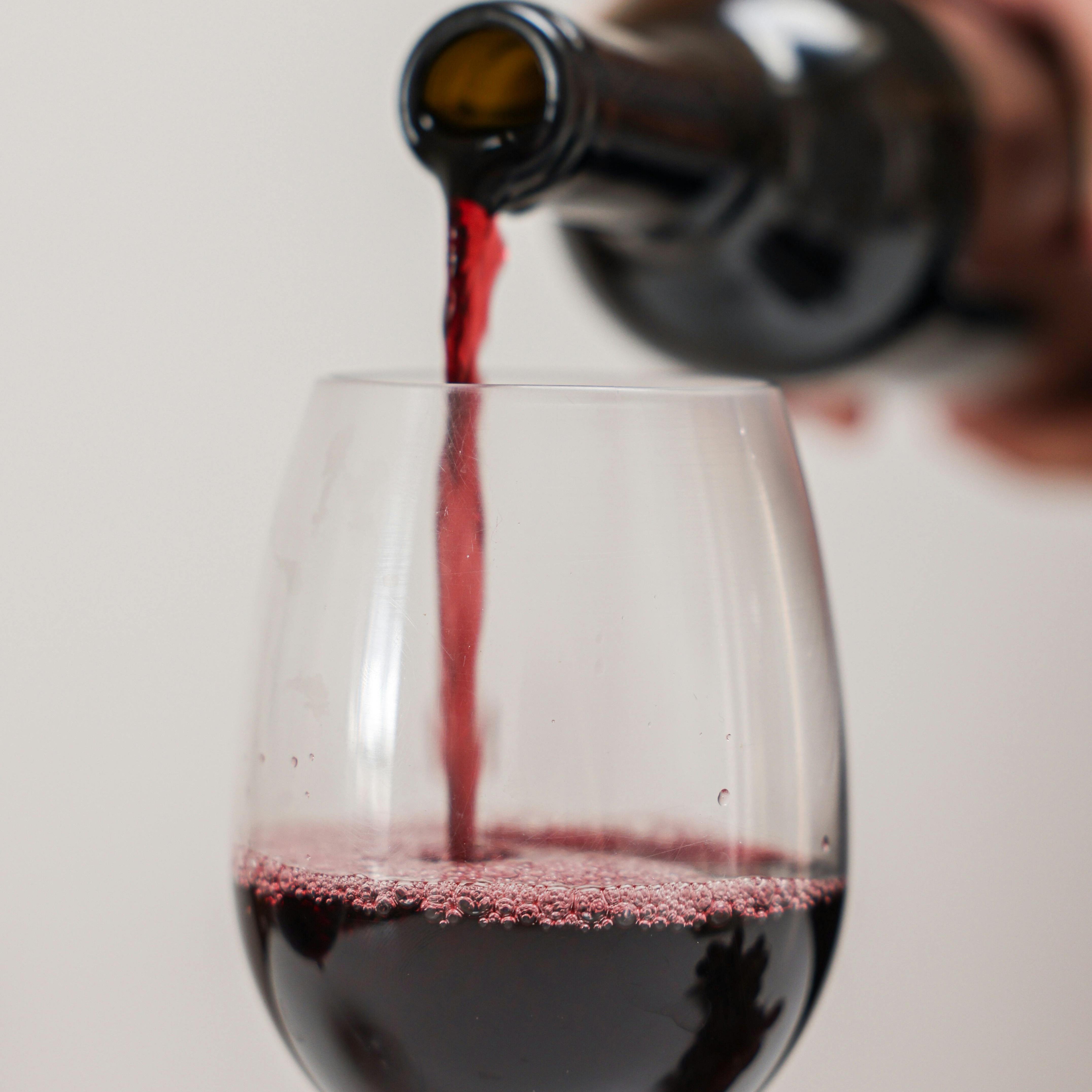 Sommelier pouring a deep ruby Burgundy into a crystal stem glass — close up against a soft warm backdrop